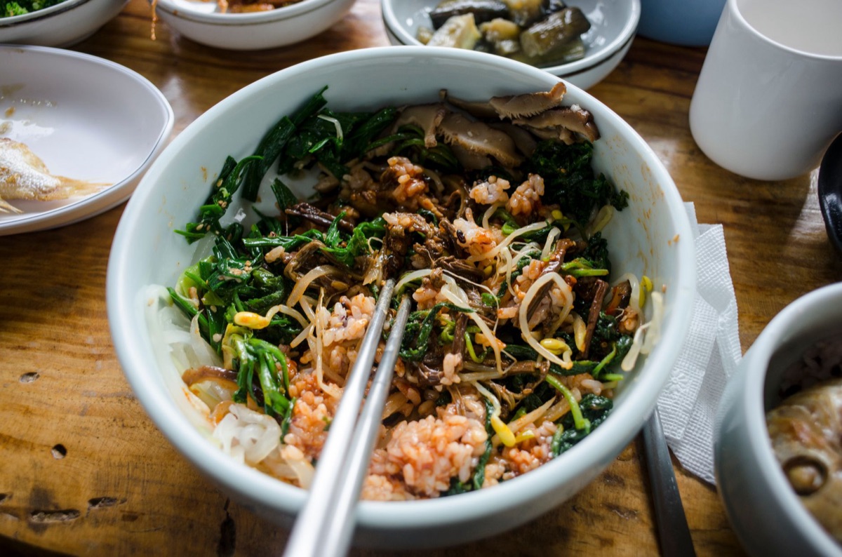 白碗裡盛著飯、菠菜、豆芽、香菇，並放著筷子的拌飯