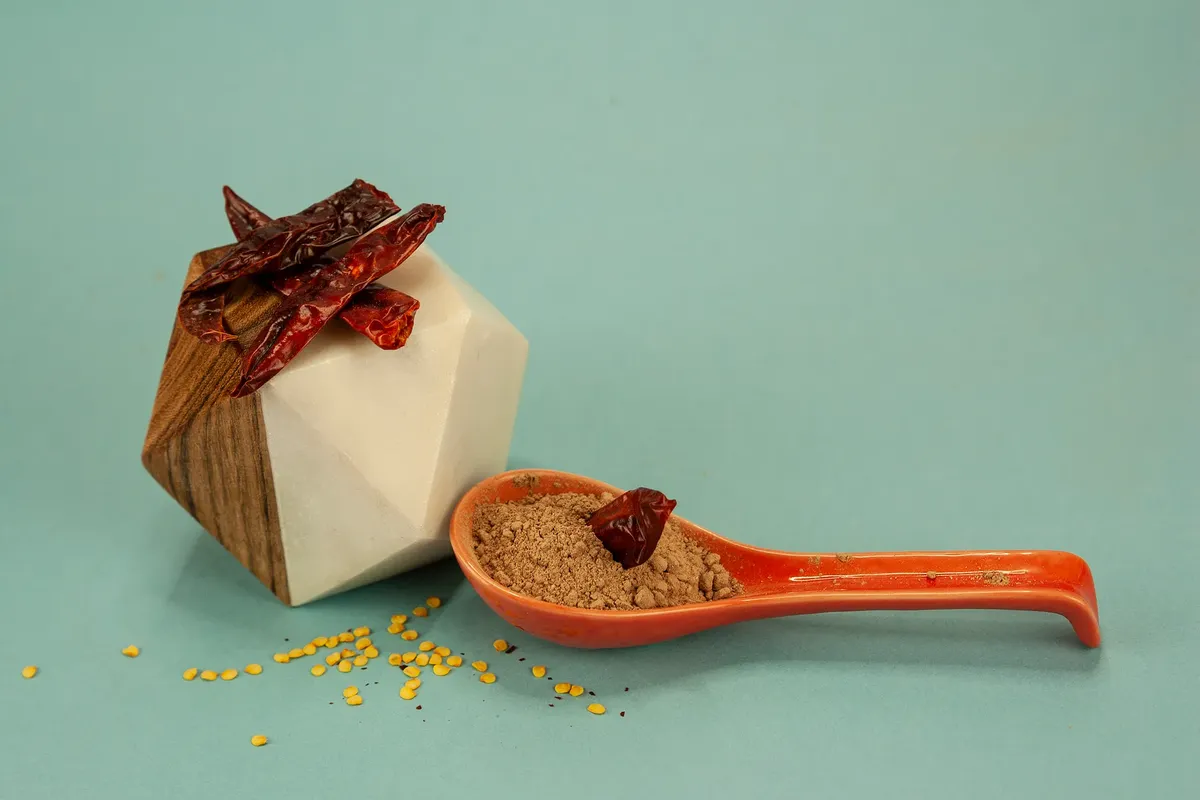 A stylistic photo of dried red chilies and spice powder arranged creatively on a colored background.
