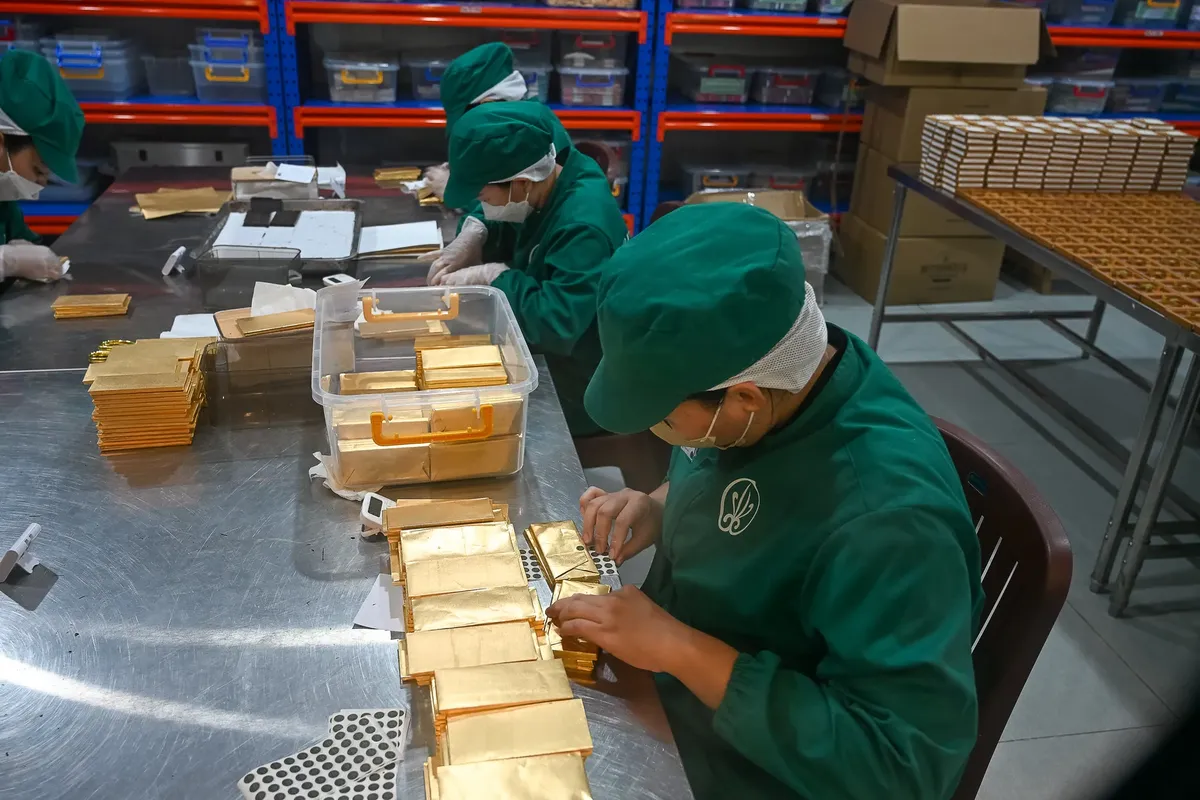 A group of workers in a Vietnamese factory packaging chocolate bars with gold foil.