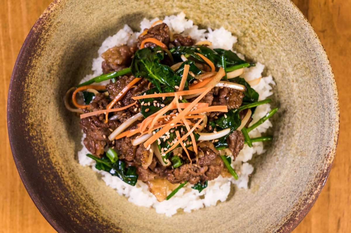 Un chef coreano che prepara un piatto stagionale con ingredienti brillanti in una luce studio soffusa